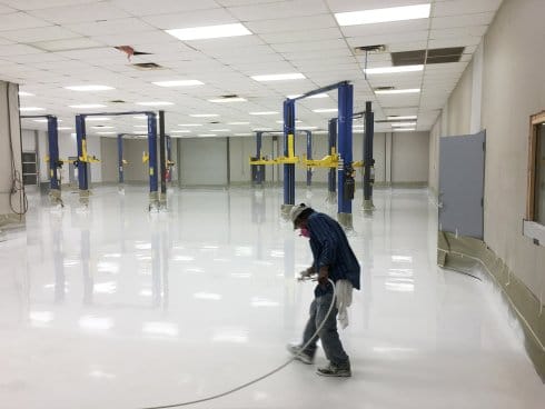 A worker is spraying white epoxy on a big commercial floor to finish epoxy flooring